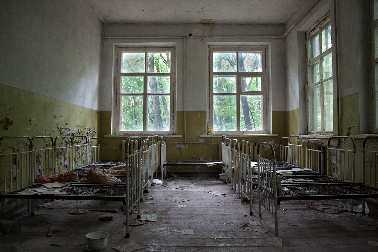 Peeling yellow walls and iron cots in an abandoned Pripyat nursery