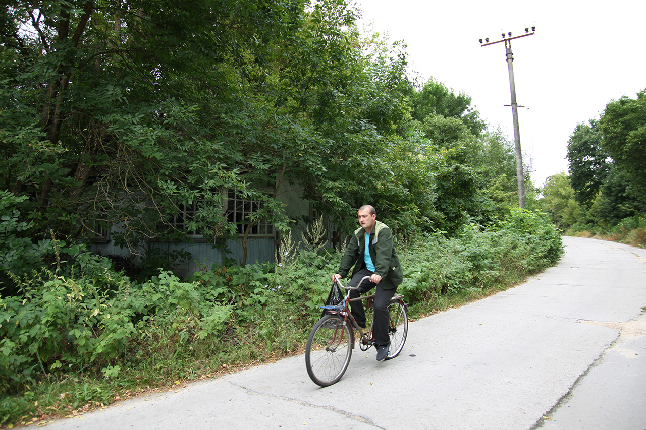 Man cycling down an overgrown road past an abandoned house in the Chernobyl zone