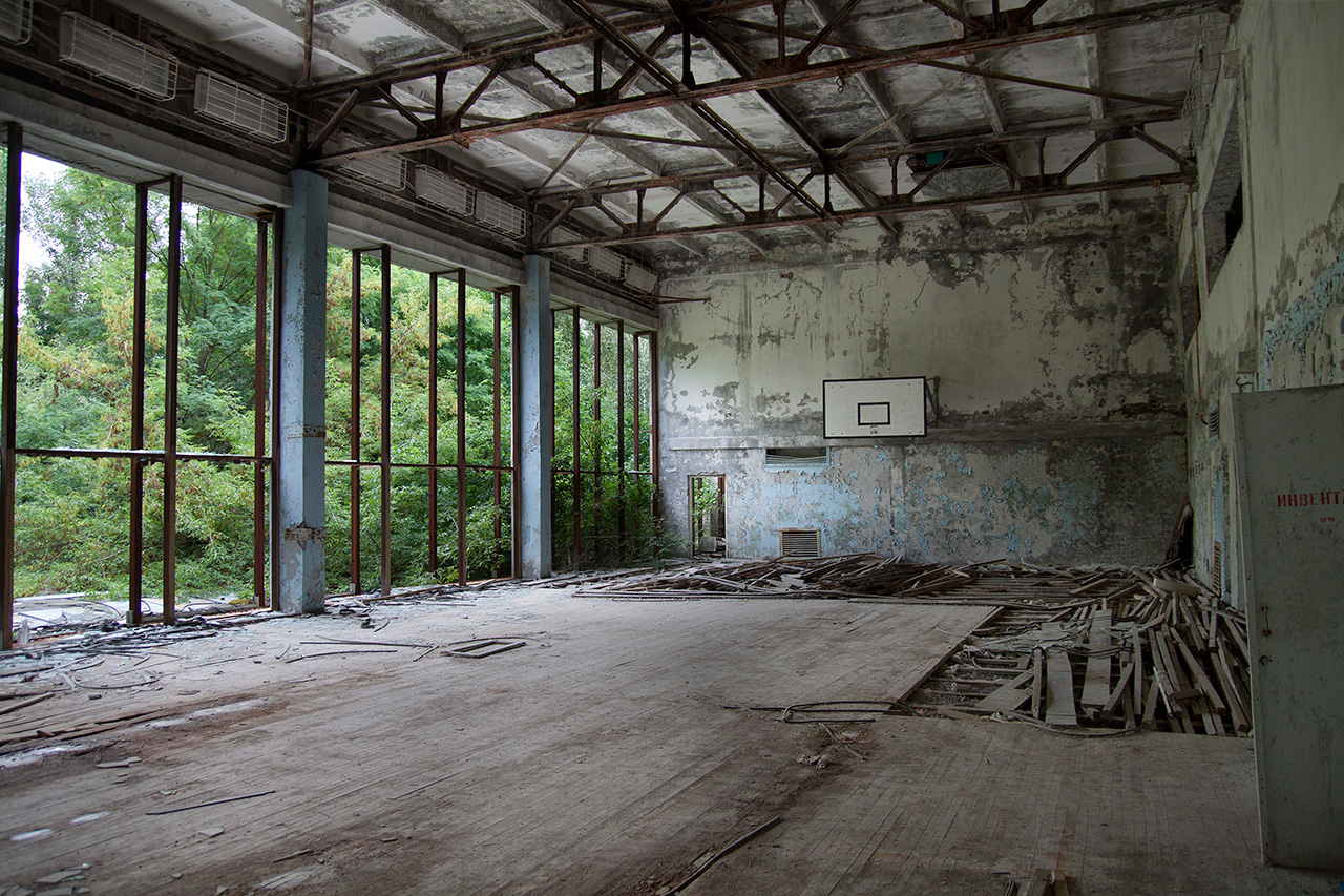 Derelict school gymnasium with torn floorboards and basketball hoop in Pripyat