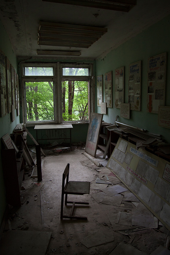 Abandoned classroom with scattered posters and a lone chair by the window in Pripyat
