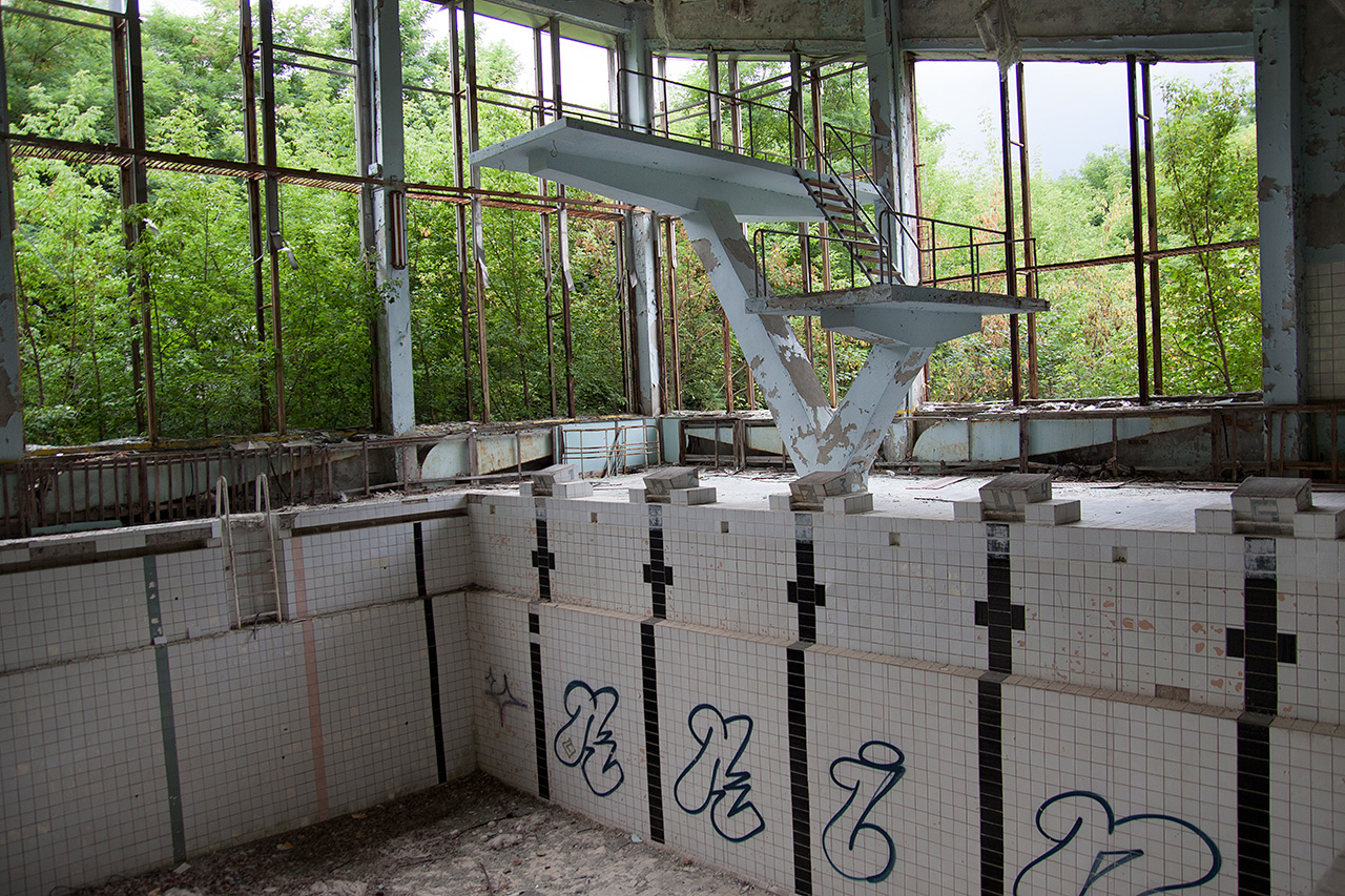 Derelict swimming pool with diving board reclaimed by trees in Pripyat