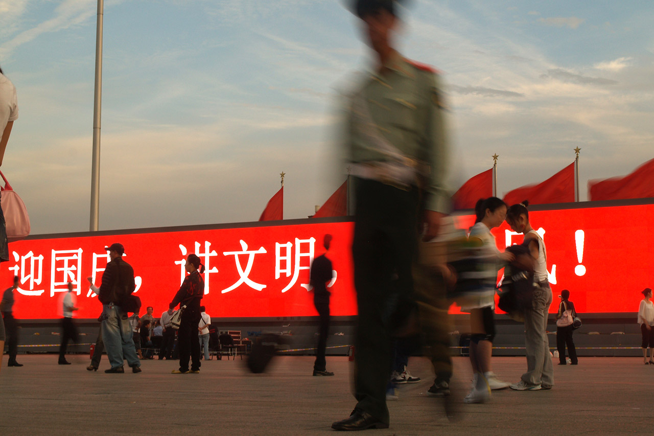 Soldier in silhouette walking past red LED banner in Tiananmen Square, Beijing
