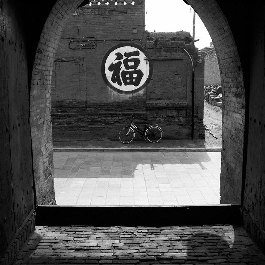 View through an arched gate of a Fu character mural and bicycle, Pingyao