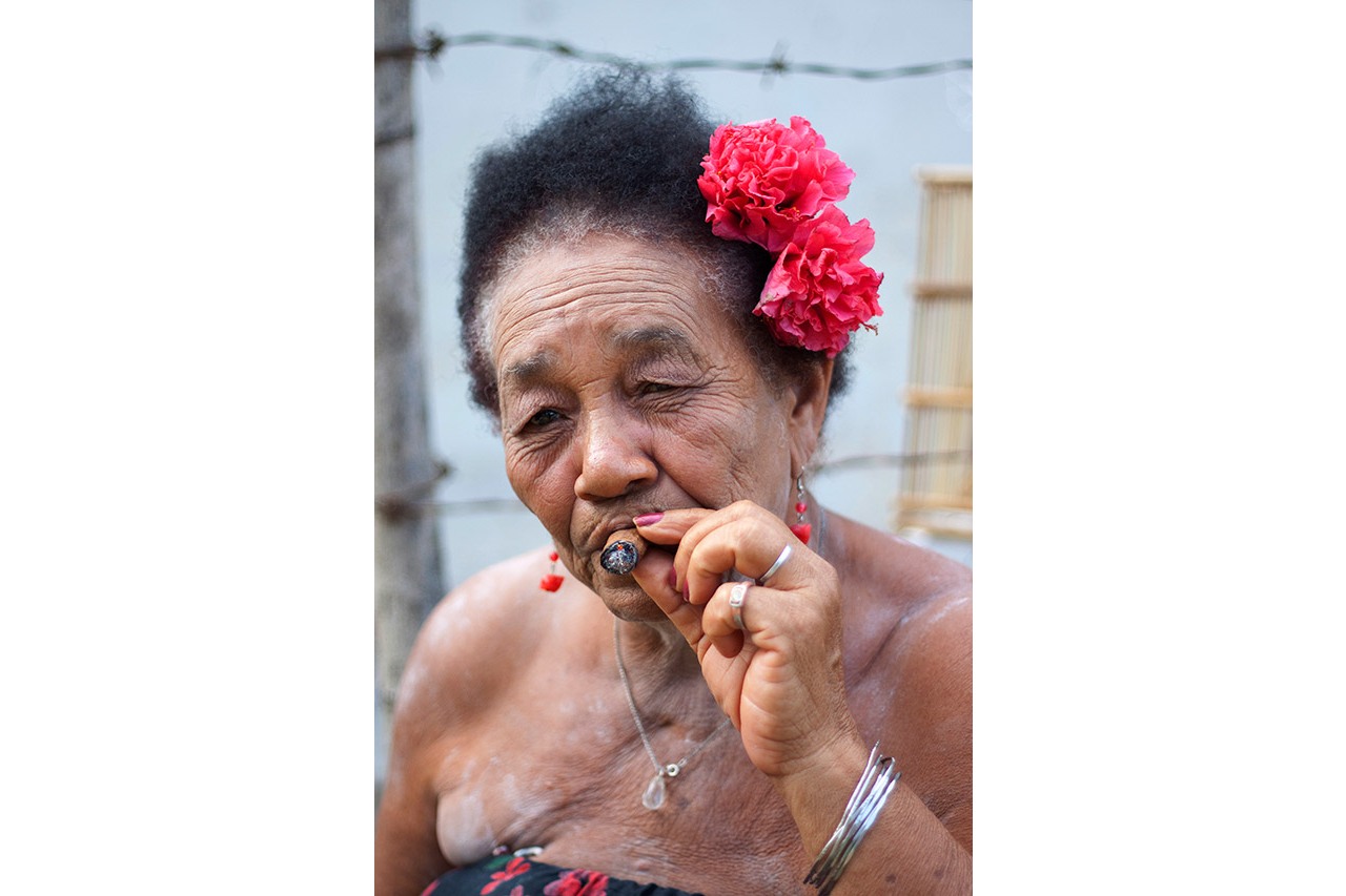 Portrait of an elderly Cuban woman smoking a cigar with red flowers in her hair