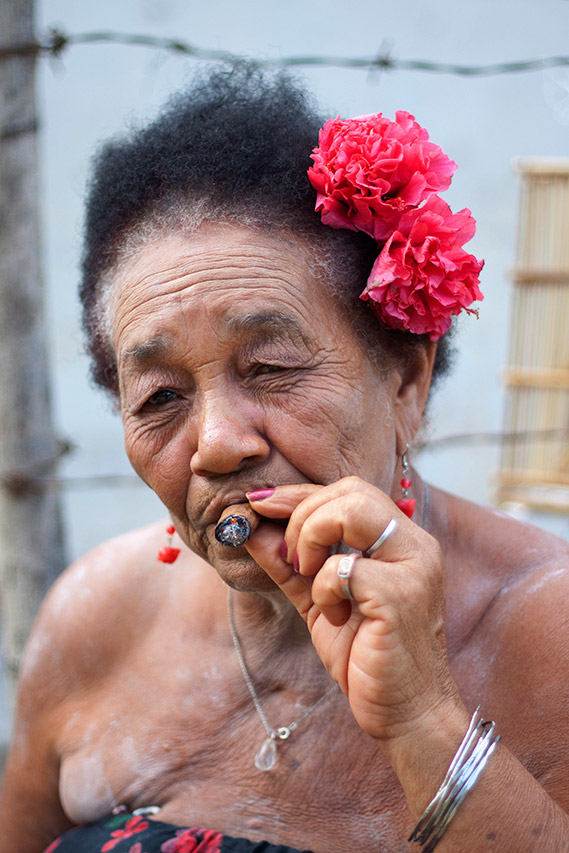 Portrait of an elderly Cuban woman smoking a cigar with red flowers in her hair