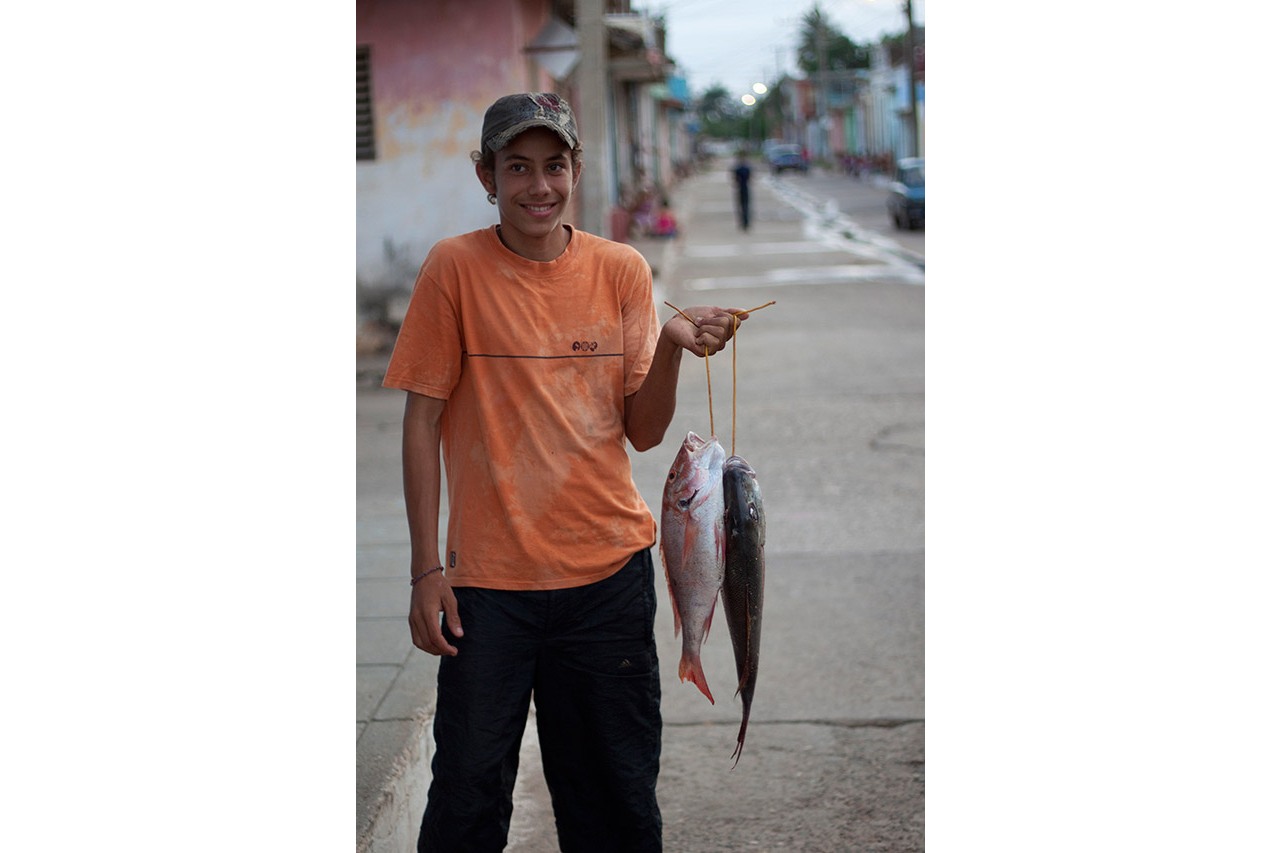 Young Cuban boy in an orange shirt holding freshly caught fish in the street