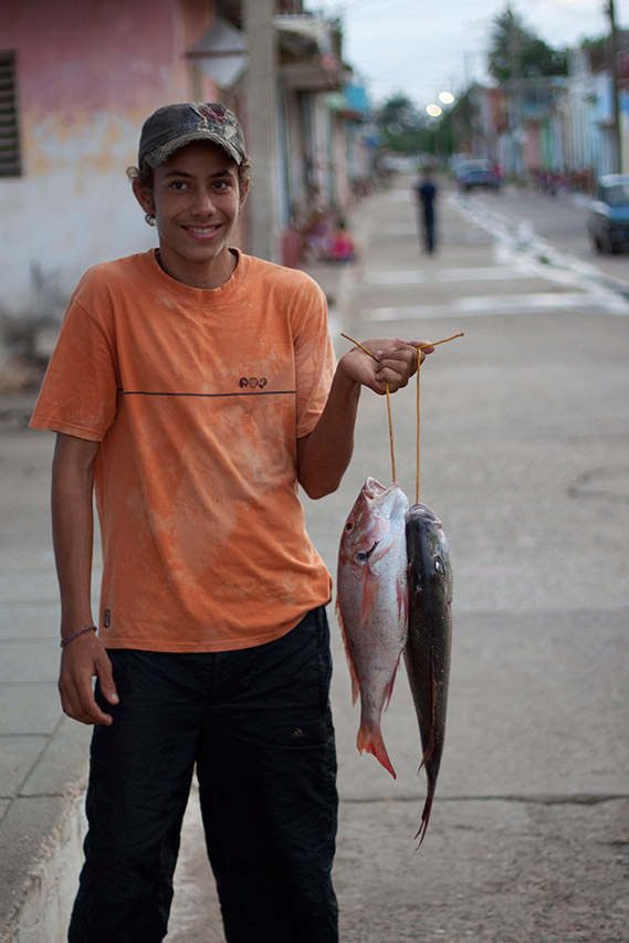 Young Cuban boy in an orange shirt holding freshly caught fish in the street