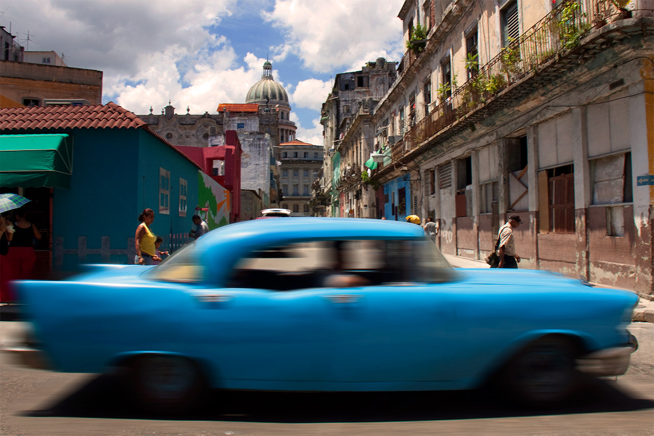 Blue vintage car speeding through Old Havana with the Capitol dome behind, Cuba