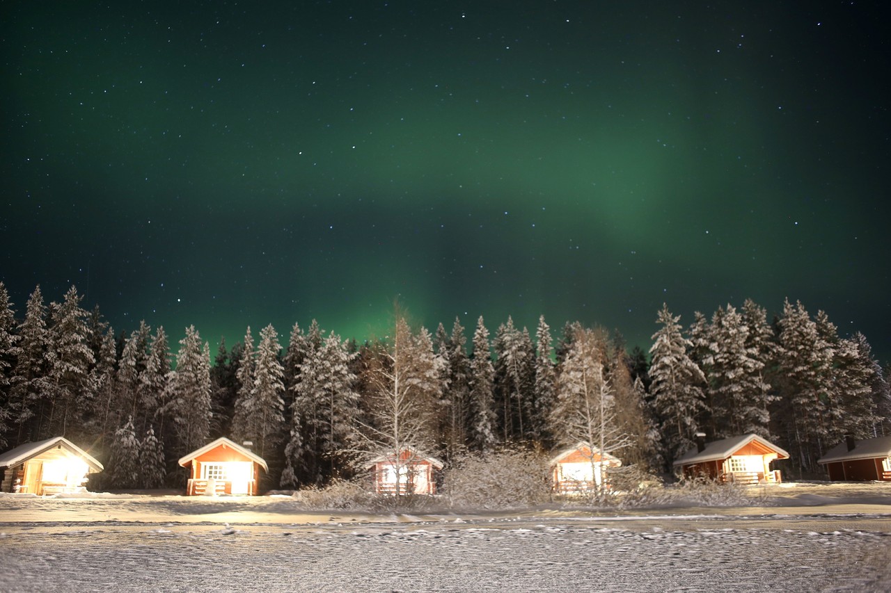 Northern lights over snow-covered cabins and forest in Lapland