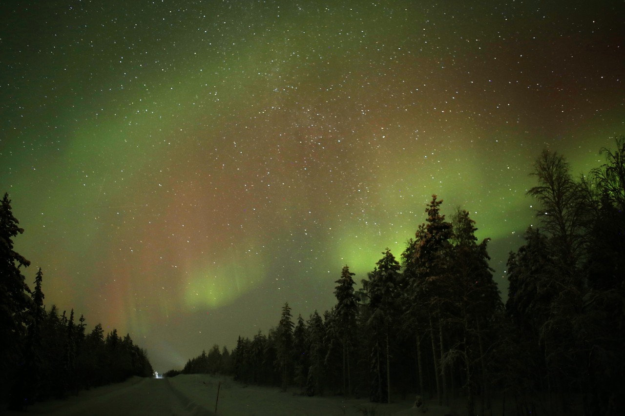 Aurora and Milky Way over a snowy forest road in Lapland
