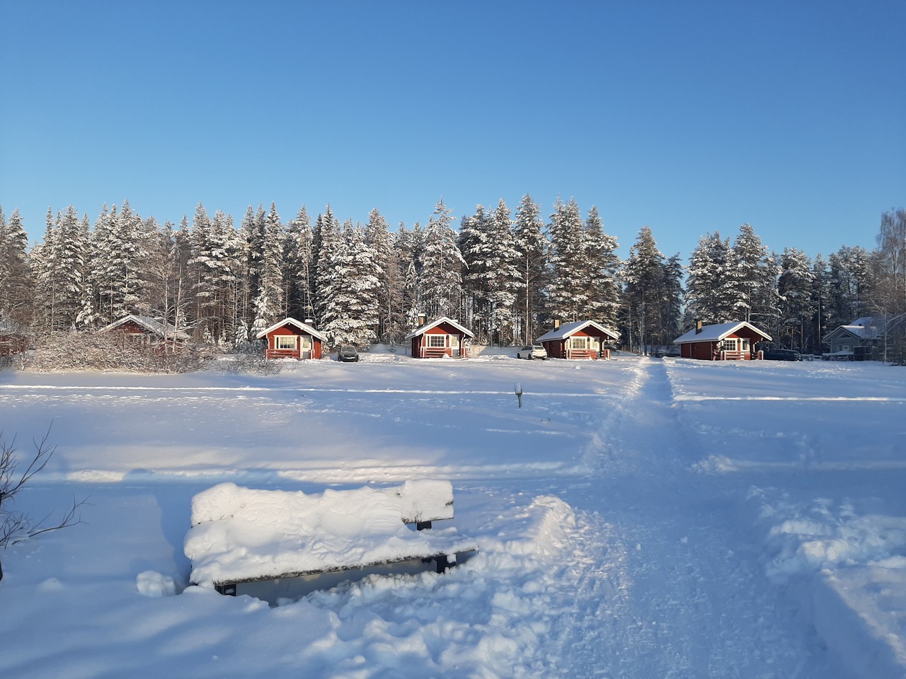 Red wooden cabins across a frozen lake under blue winter sky