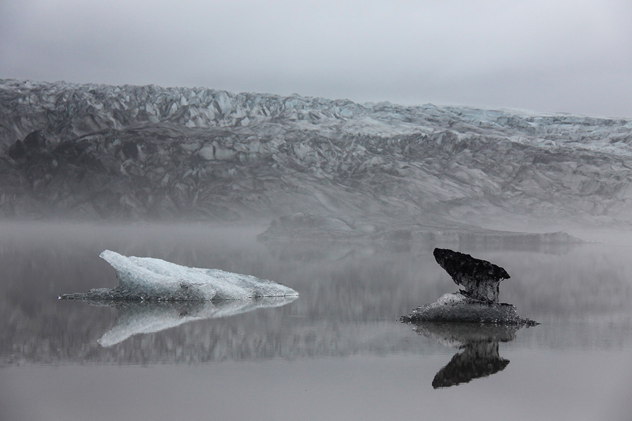 Foggy glacier with ice reflections in still water