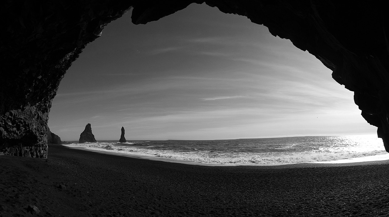 View from inside a sea cave at Reynisfjara framing the black sand beach and Reynisdrangar stacks