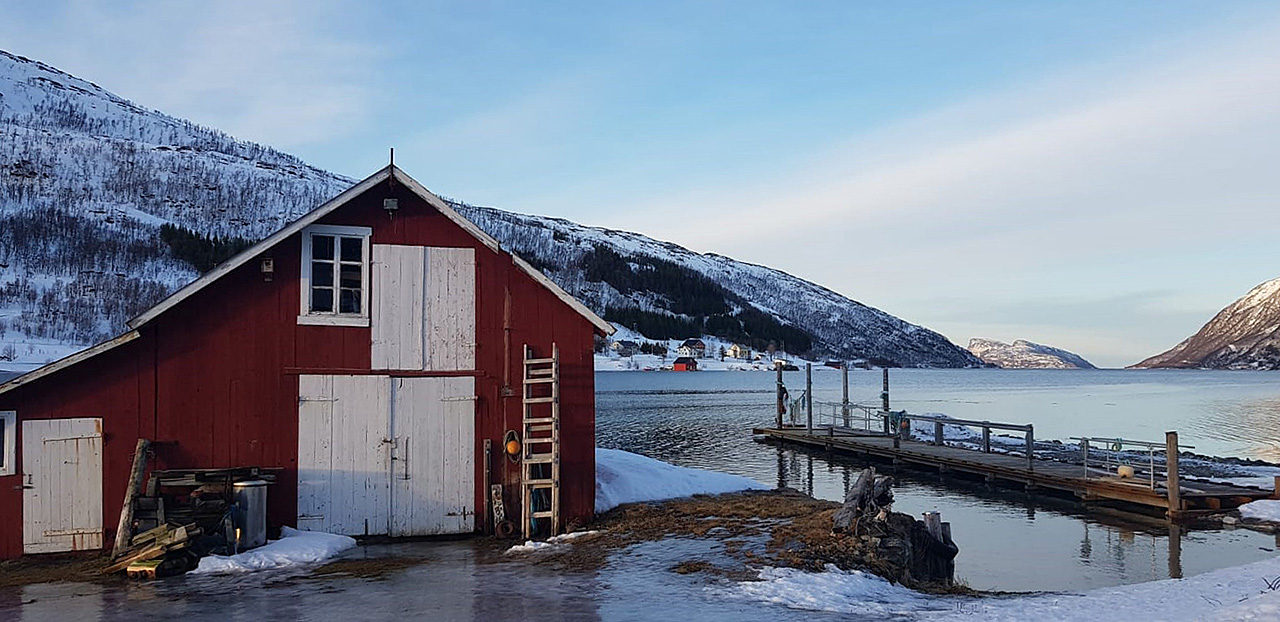 Red wooden boathouse and wooden pier on a calm Norwegian fjord
