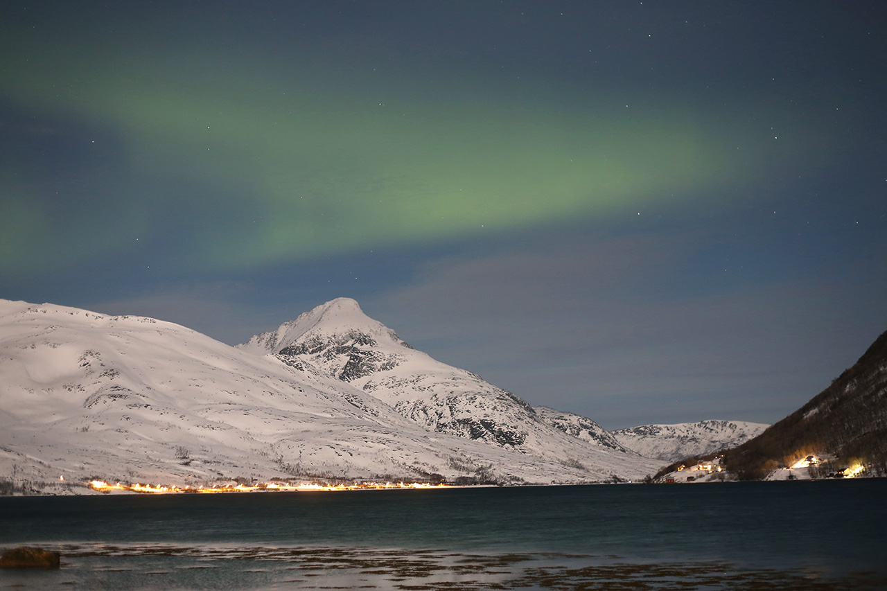 Green aurora above a snow-capped peak and fjord at night, Tromsø