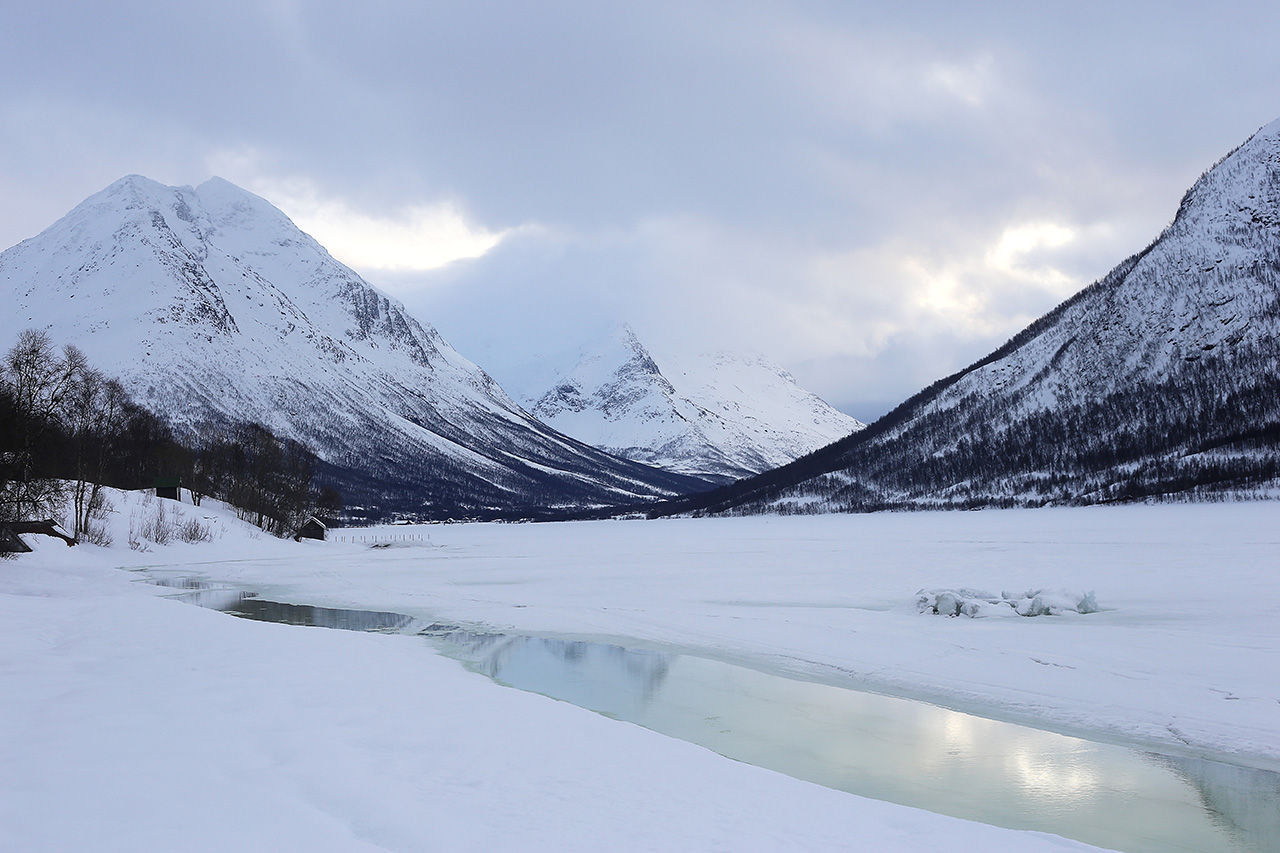 Snow-covered valley with icy stream and rugged peaks, Tromsø