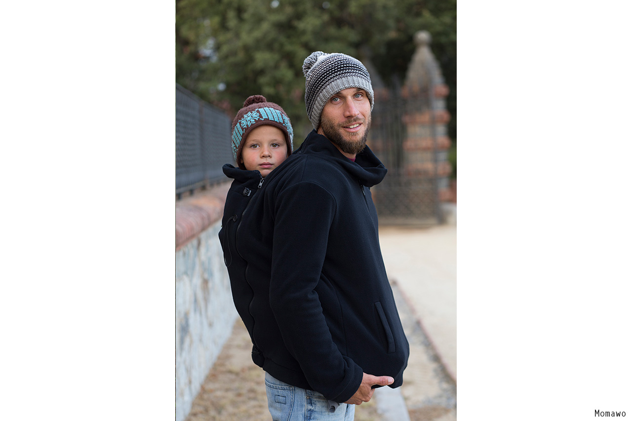 Father carrying child on back, both wearing knit hats