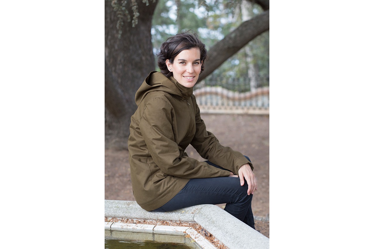 Woman in olive jacket sitting on stone fountain — Momawo