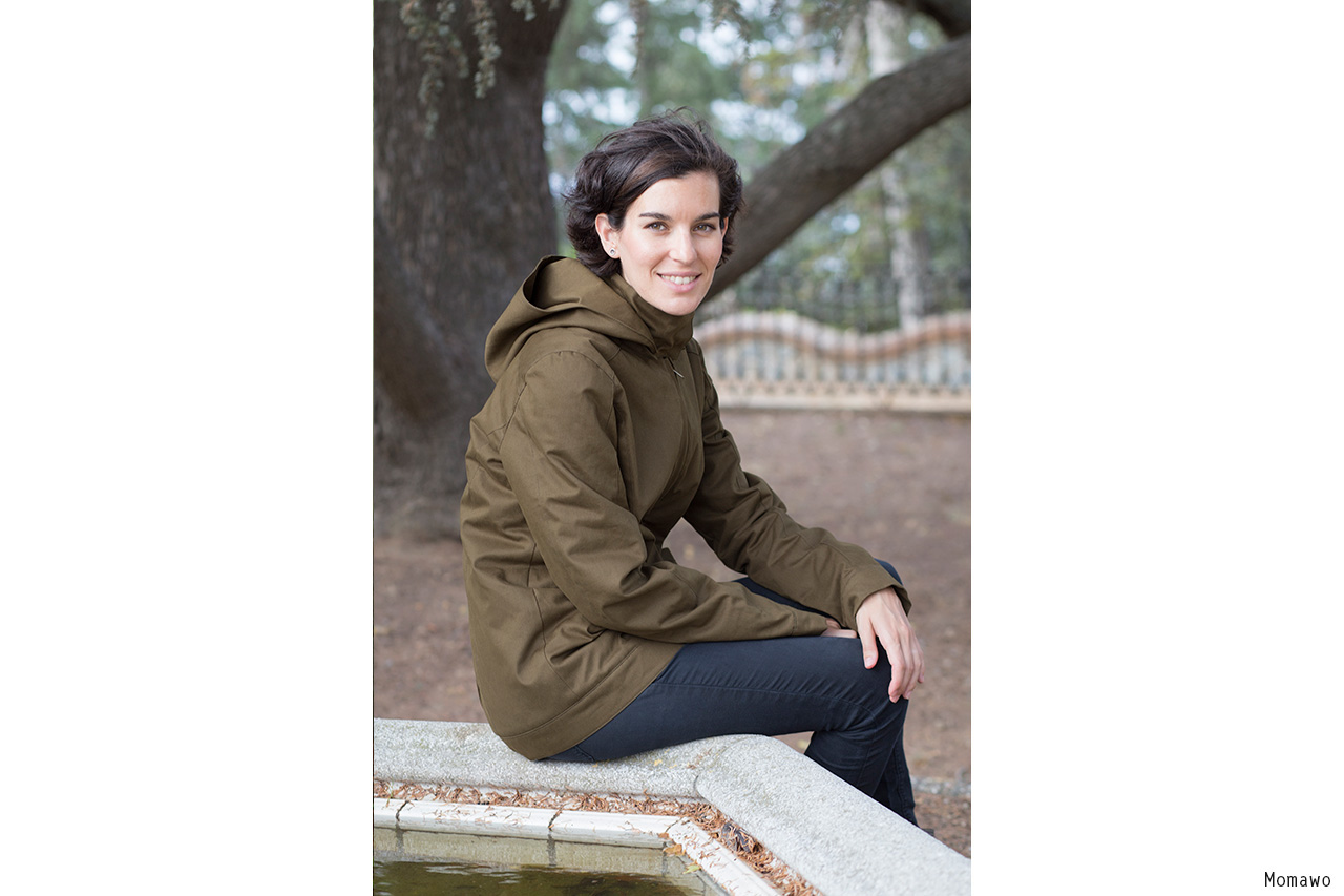 Woman in olive jacket sitting on stone fountain