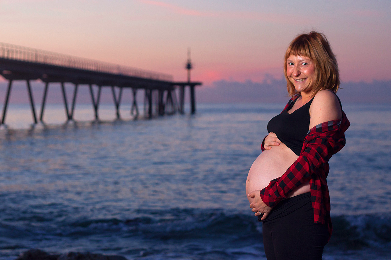 Pregnant woman at sunset by the beach pier