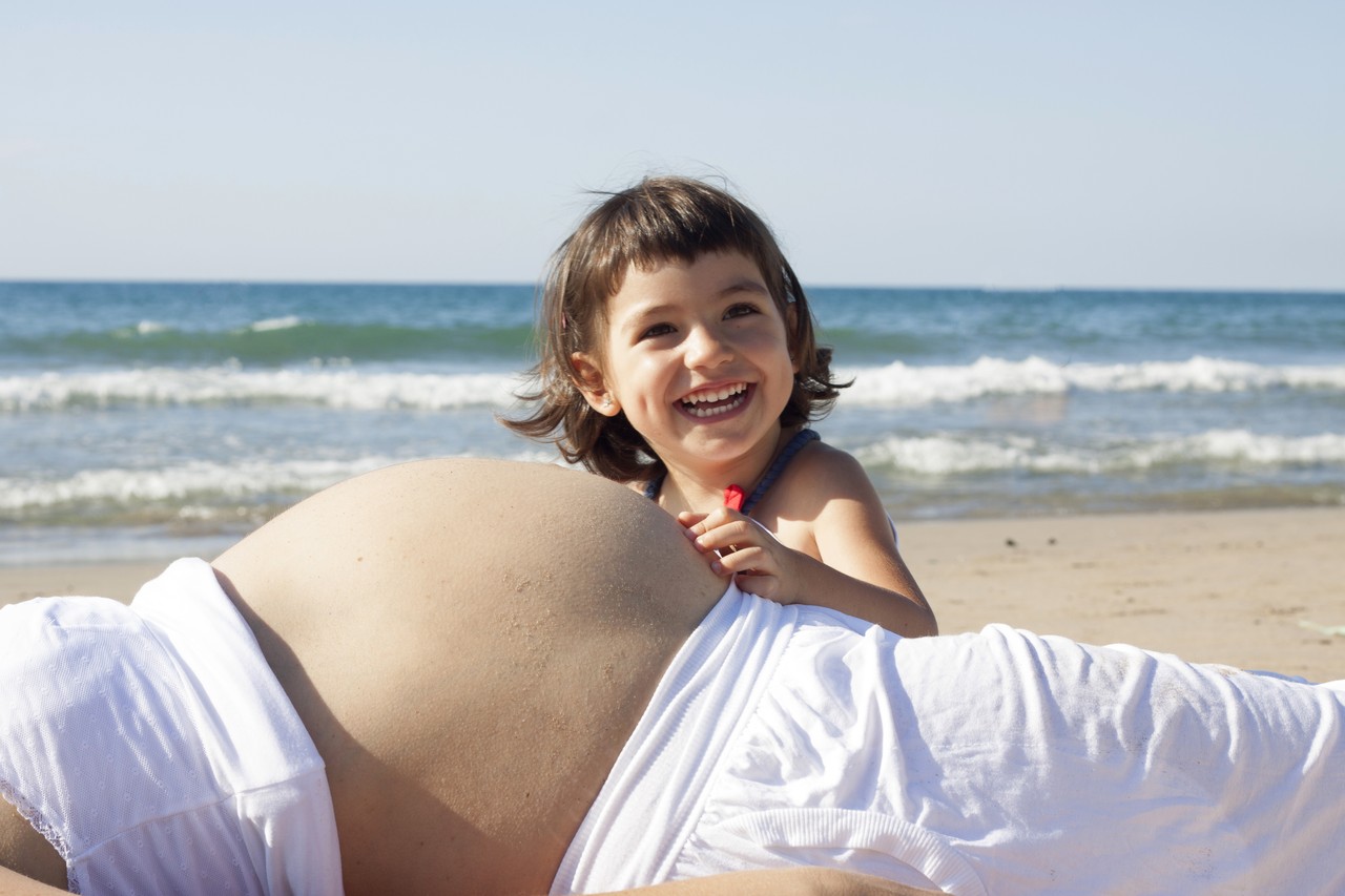 Child smiling against pregnant mother's belly at the beach