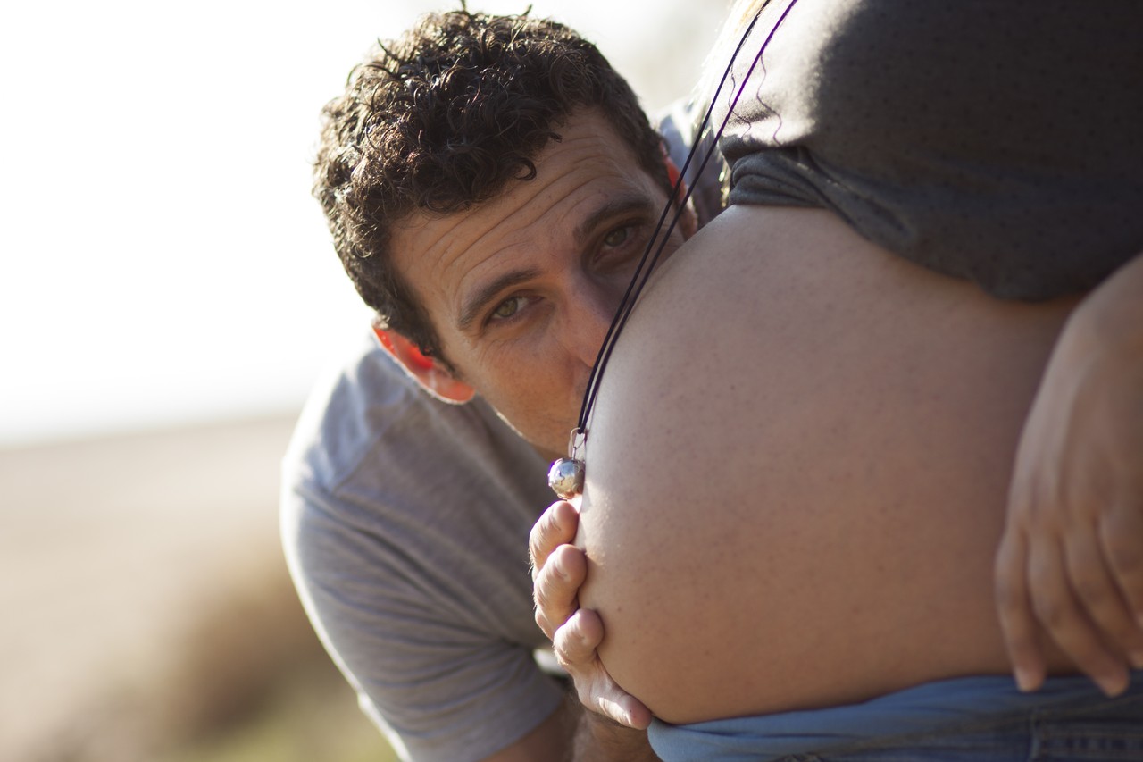 Father-to-be tenderly kissing his partner's pregnant belly outdoors