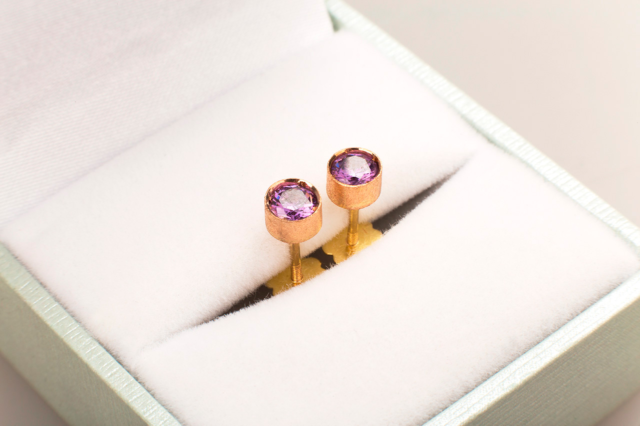 Pair of rose gold earrings with purple gemstones in box