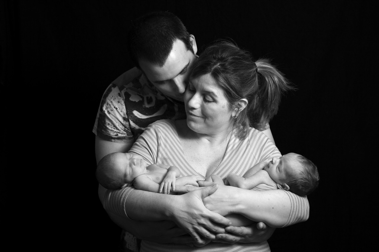 Black and white studio portrait of parents holding newborn twins