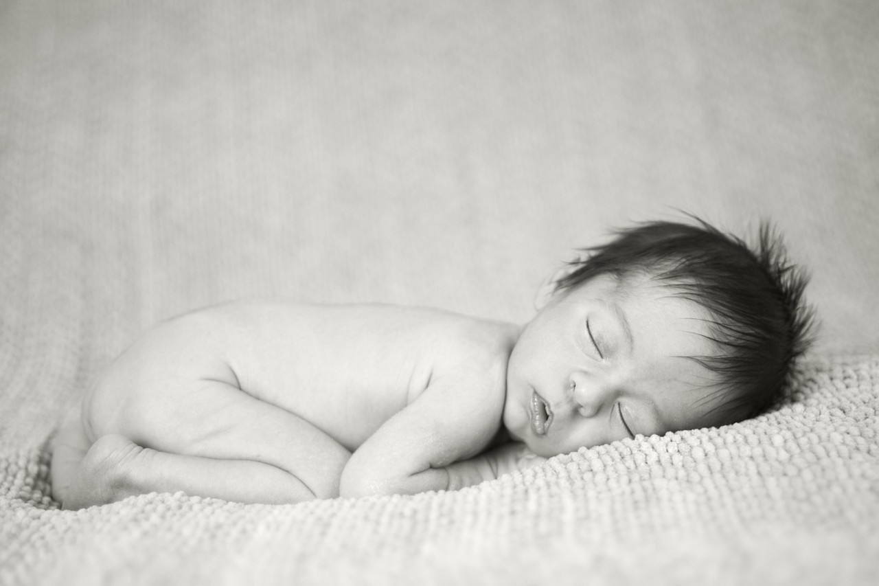 Black and white studio portrait of newborn baby sleeping on a knit blanket