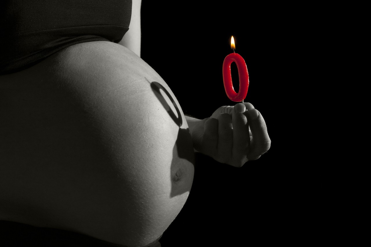 Black and white maternity portrait with a red zero-shaped candle casting its shadow on the belly