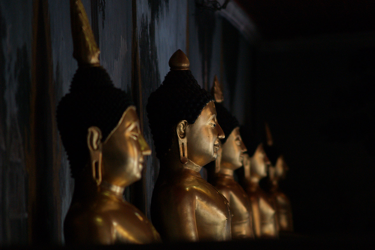Row of golden Buddha statues glowing in a dark temple hall, Thailand