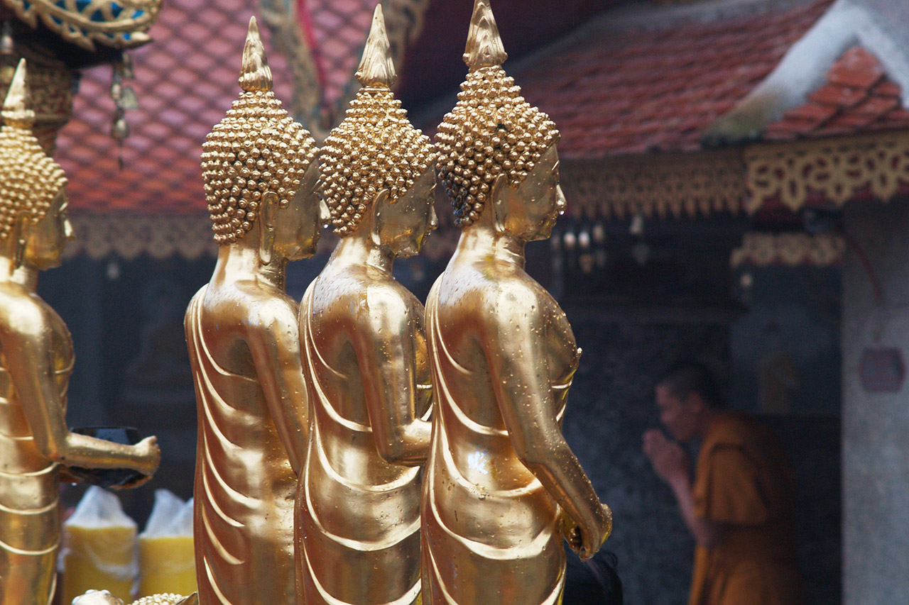 Golden Buddha statues with a monk praying behind, Wat Phra That Doi Suthep