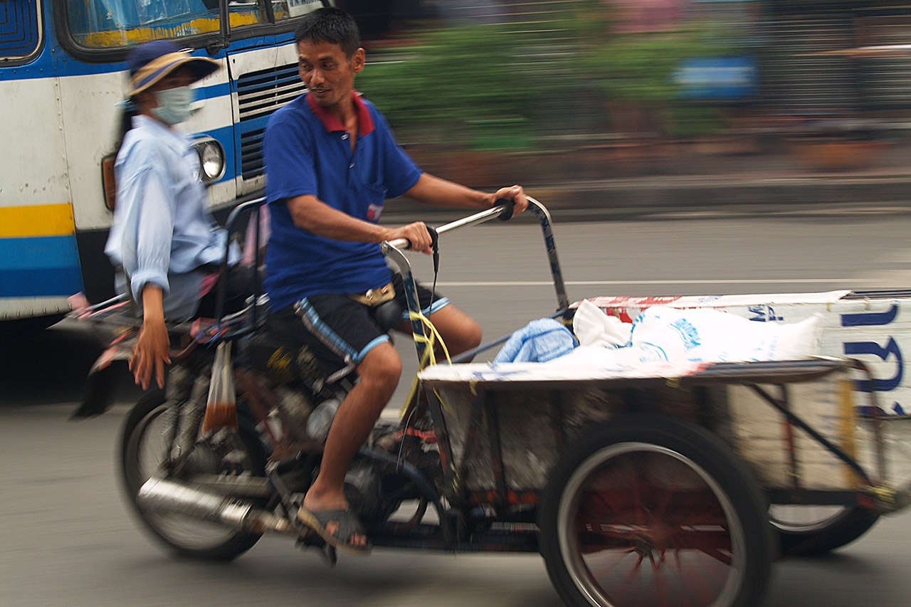 Man riding a loaded cargo tricycle through Bangkok traffic