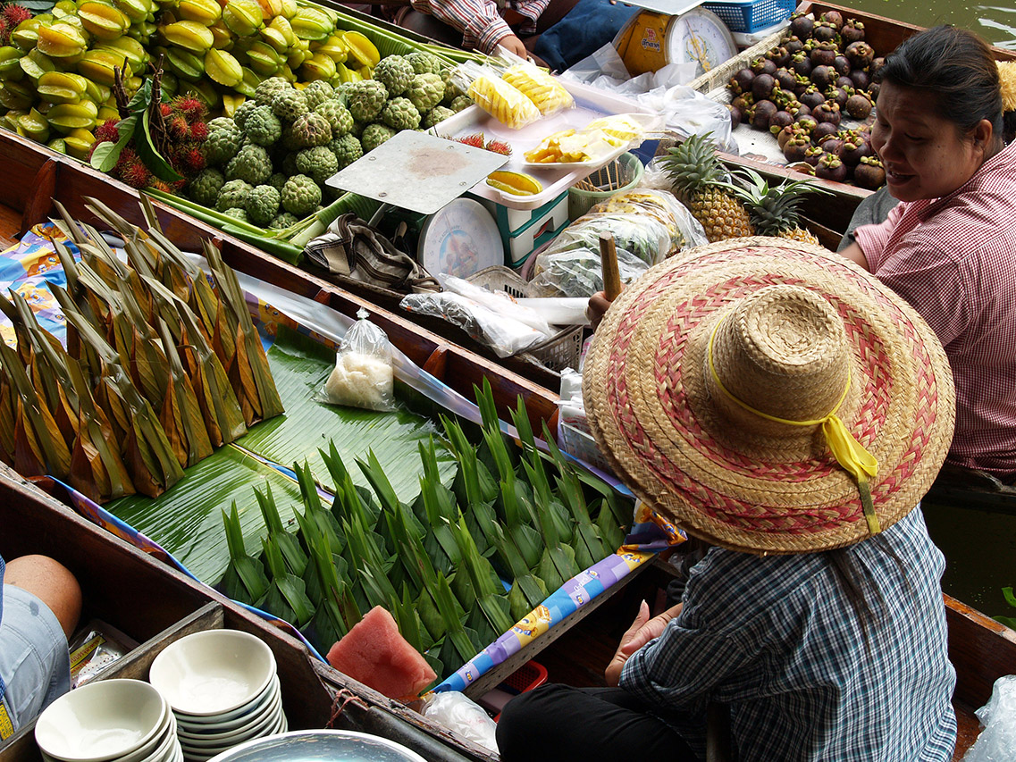 Vendor in straw hat selling tropical fruit from a boat, Thailand
