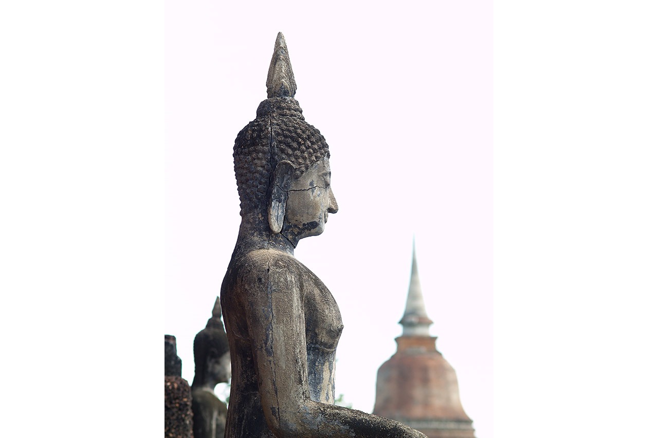 Profile of a weathered stone Buddha with distant chedi, Sukhothai