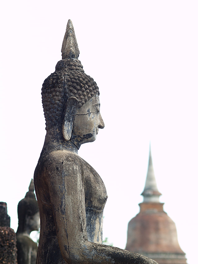 Profile of a weathered stone Buddha with distant chedi, Sukhothai