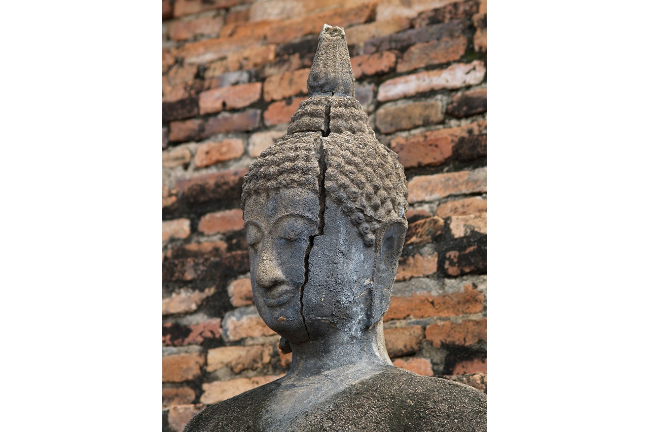 Cracked stone Buddha head against a brick wall, Ayutthaya