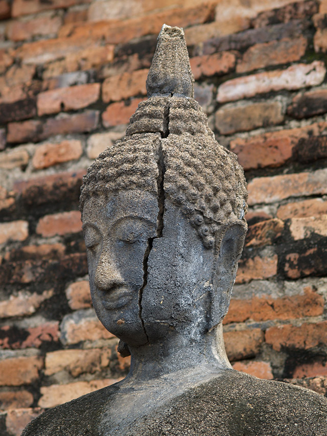 Cracked stone Buddha head against a brick wall, Ayutthaya