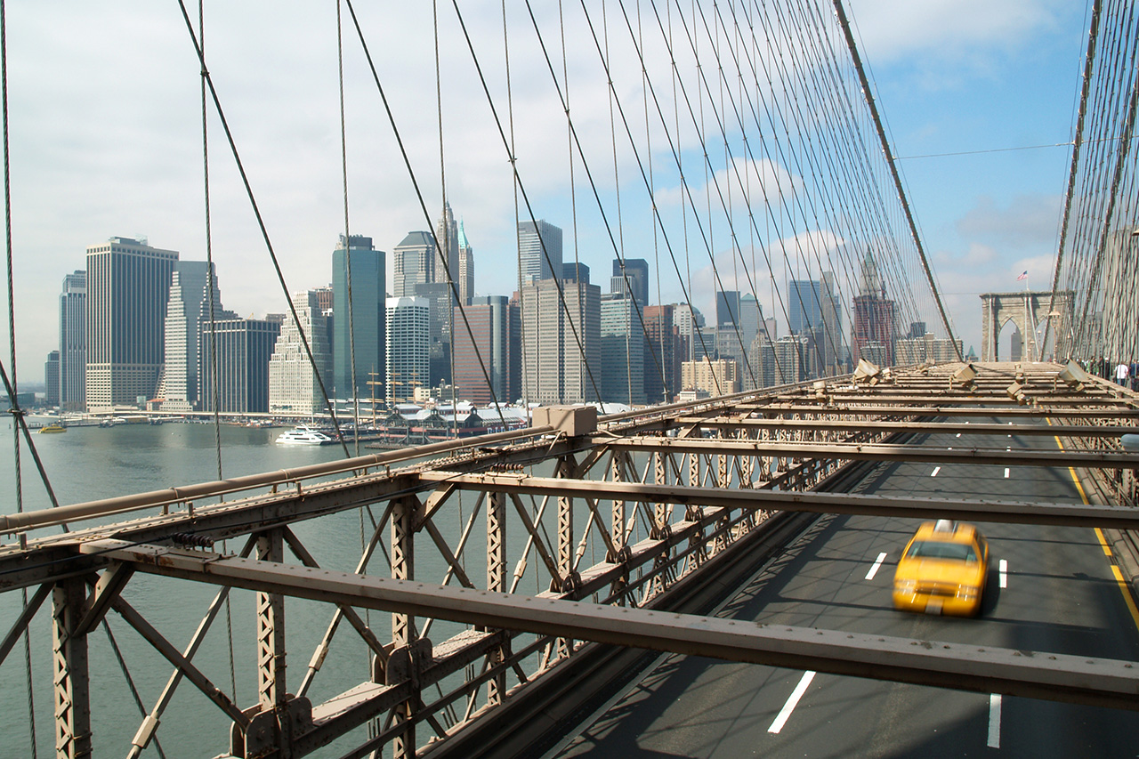 Yellow taxi crossing Brooklyn Bridge with Lower Manhattan skyline
