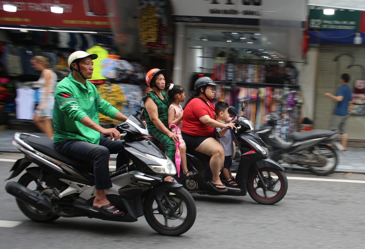 Two motorbikes carrying families speeding past shopfronts in Hanoi