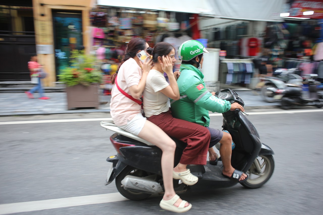 Grab driver carrying two passengers through a Hanoi street