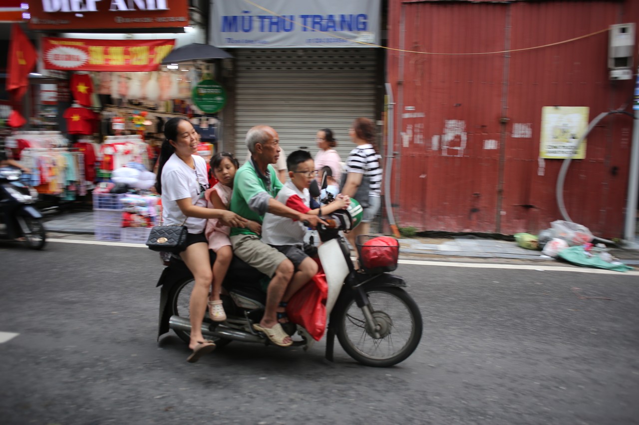 Five people sharing one motorbike in front of a red wall in Hanoi