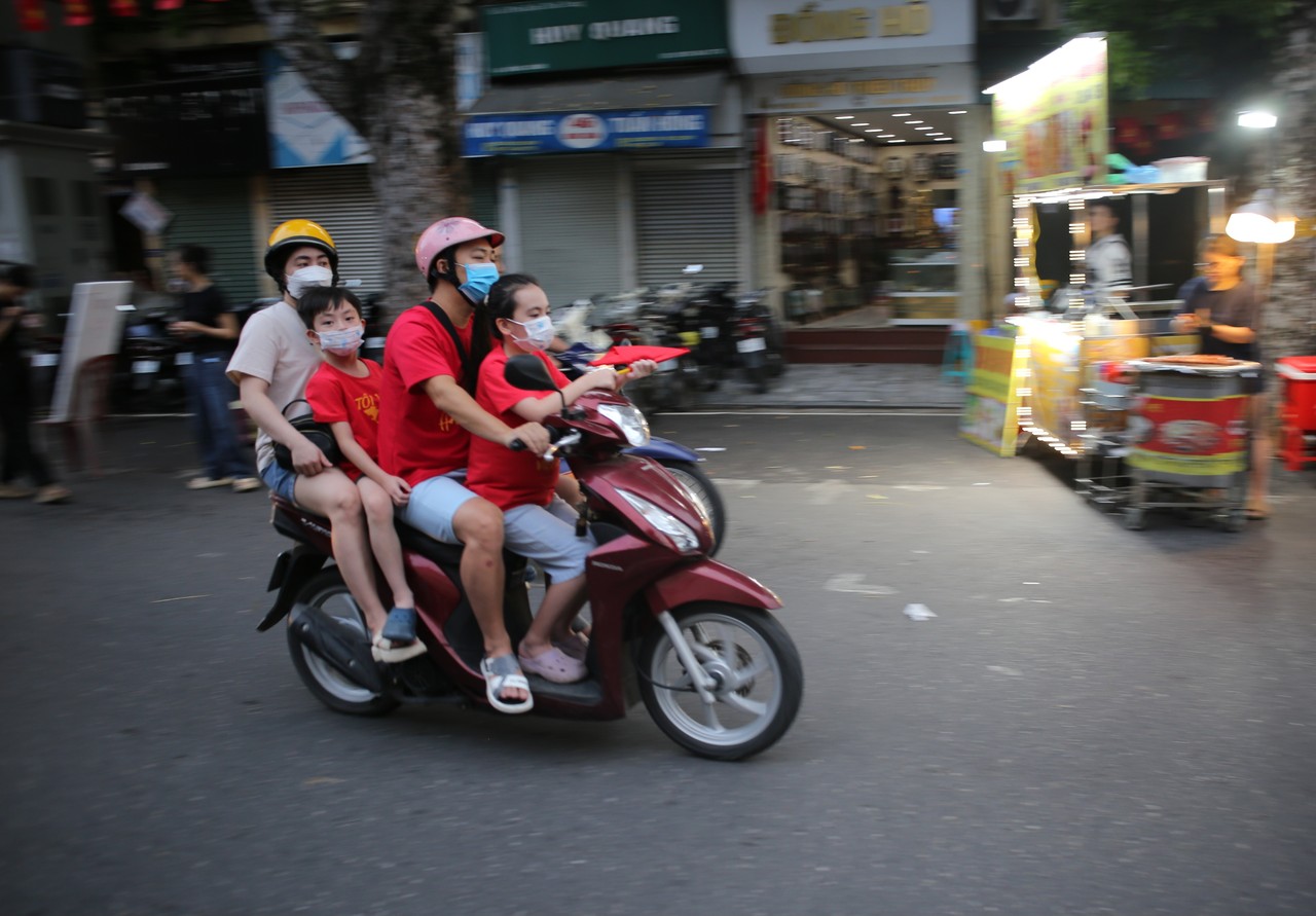 Family in red shirts riding a motorbike past a night food stall in Hanoi