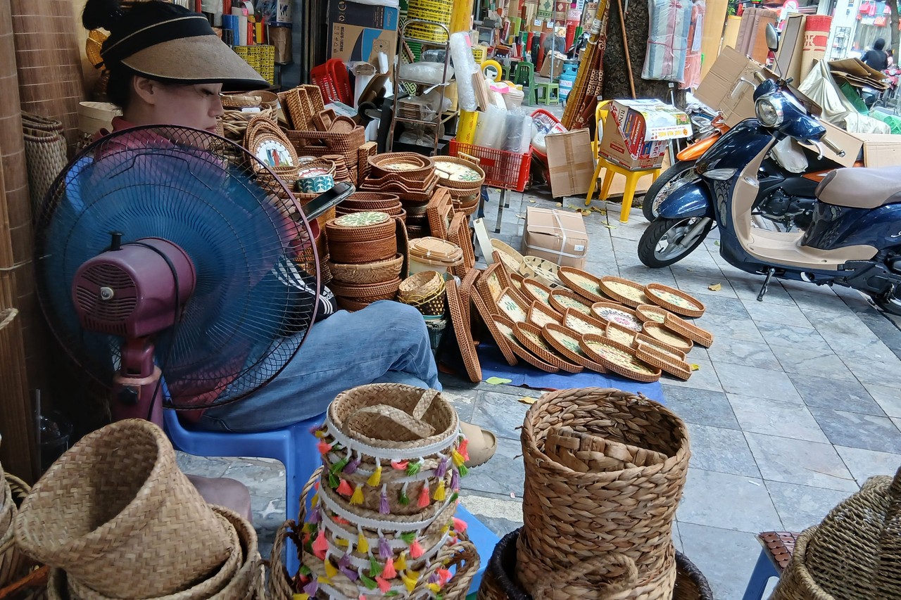 Vendor resting behind an electric fan among woven baskets in Hanoi's Old Quarter