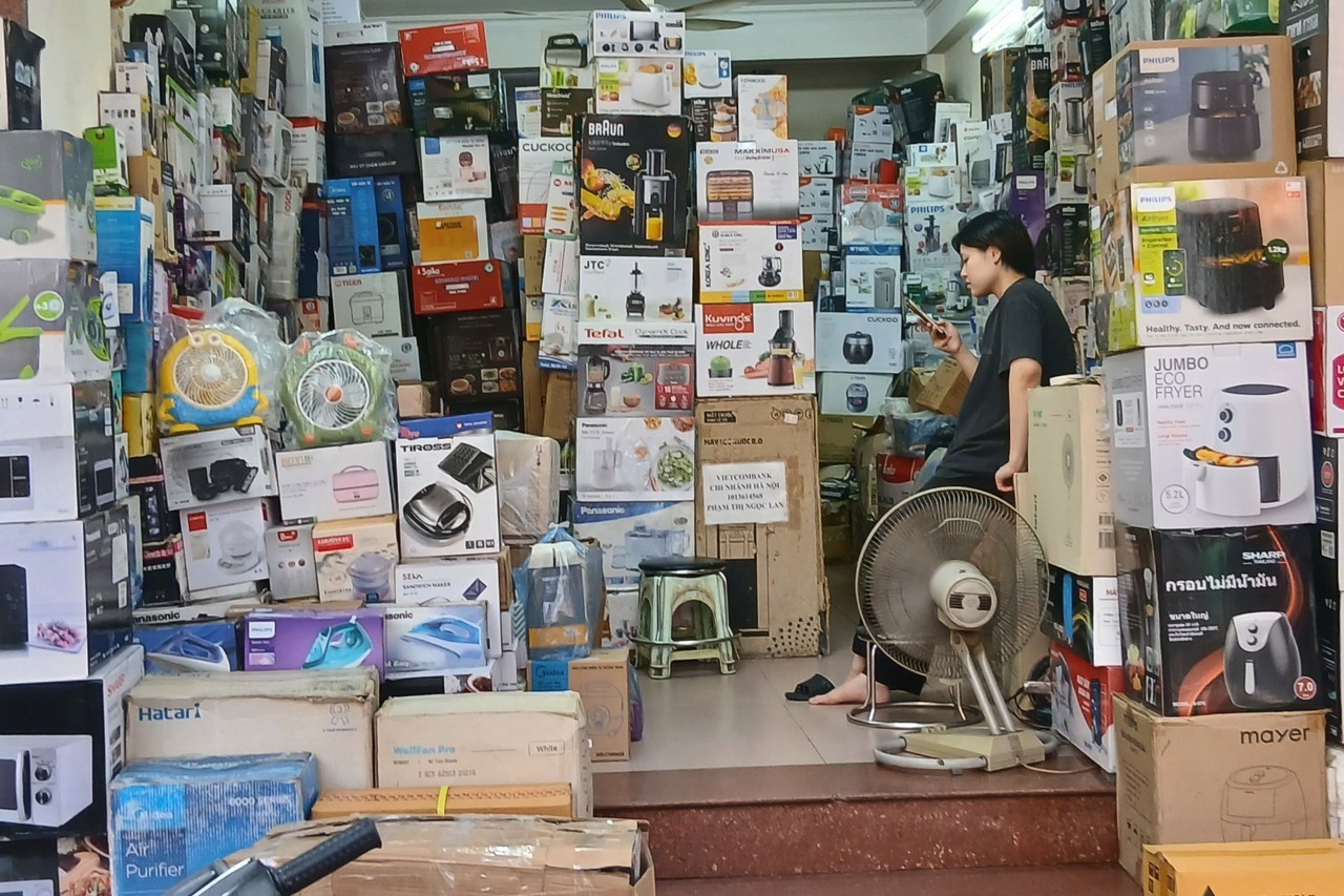 Shopkeeper on the phone inside a shop stacked with appliance boxes in Hanoi