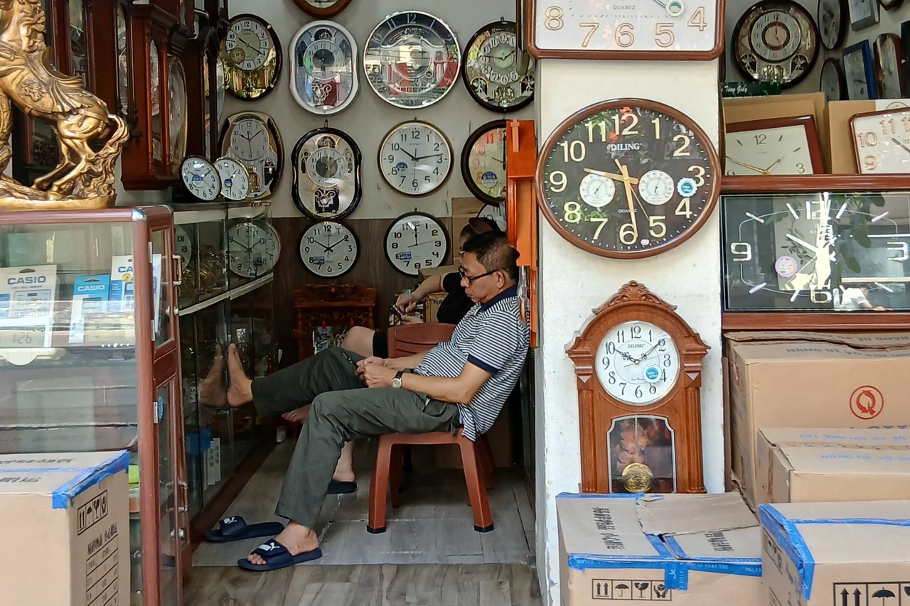 Clock seller sitting among dozens of wall clocks in a Hanoi shop