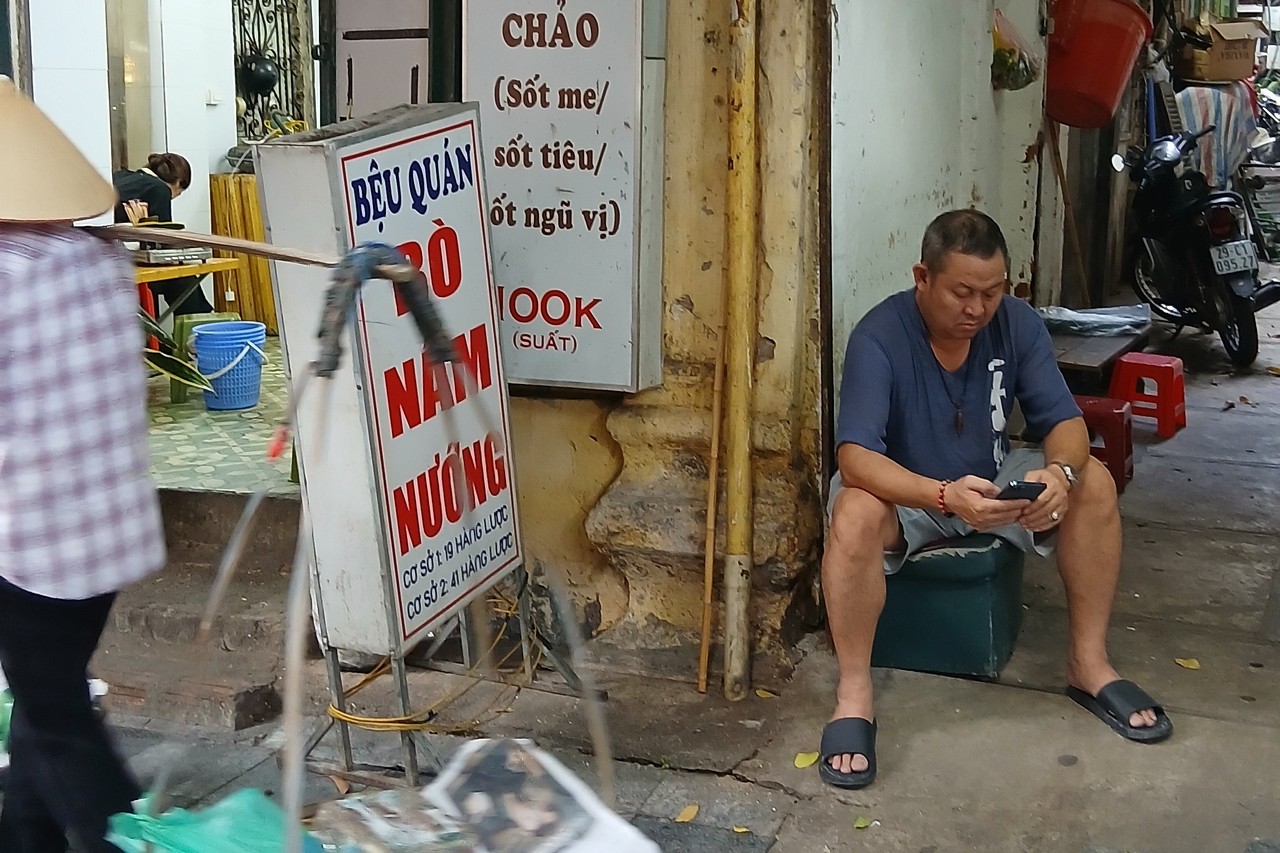 Man checking his phone beside street food signs in Hanoi