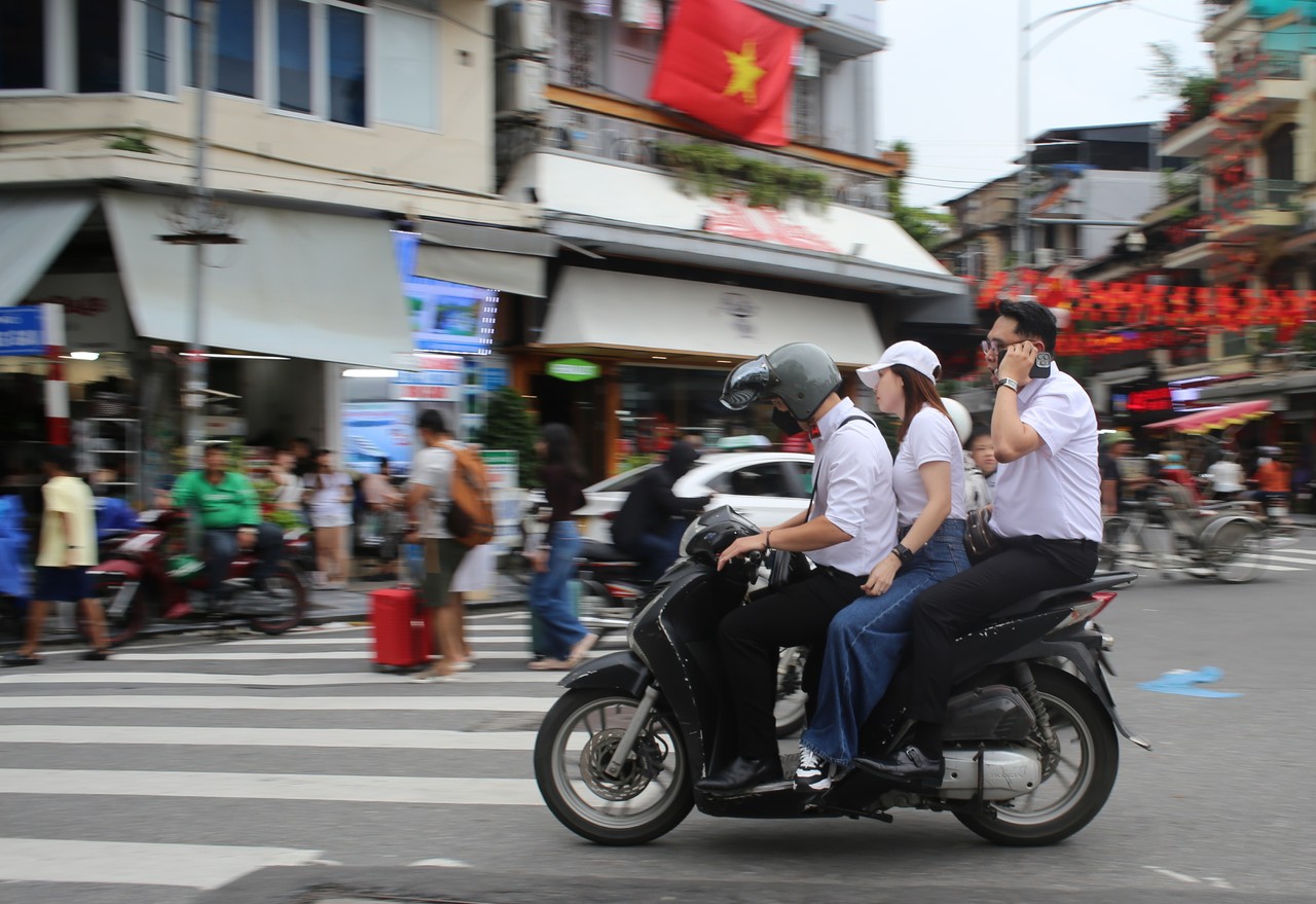 Motorbike with three riders crossing a busy Hanoi intersection
